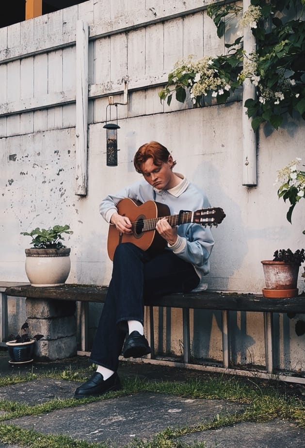 Eskil Fossum Vik spiller gitar på en benk i en bakgård, kledd i retro dress.