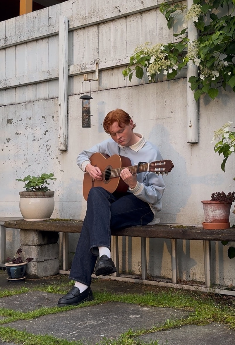 Eskil Fossum Vik spiller gitar på en benk i en frodig bakgård.